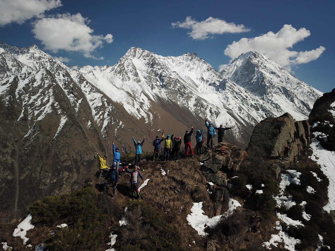 Pastors and youth leaders from Central Asia standing on a mountain ridge with snow-capped peaks, celebrating with raised arms