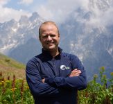 Portrait of Joel Vermillion smiling outdoors with mountains in the background
