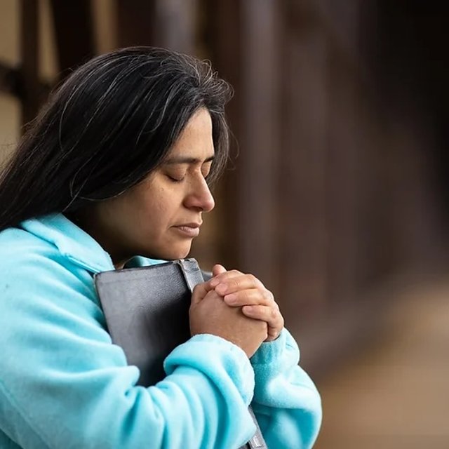 A woman praying with a Bible held to her chest